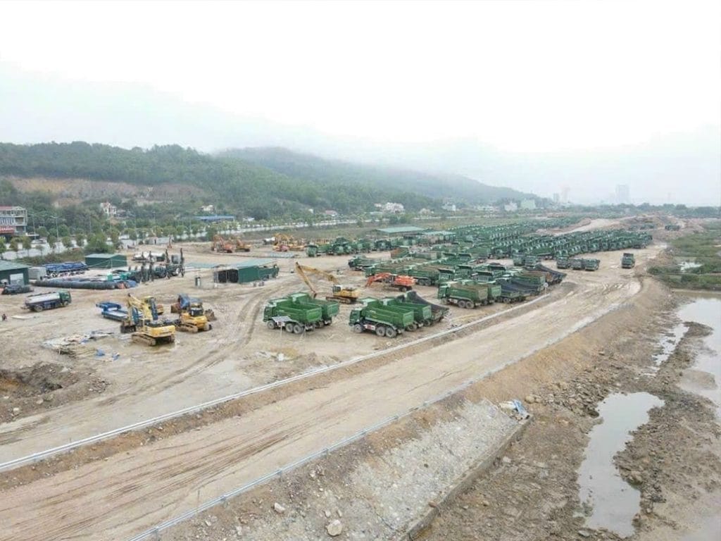 The Fullton 23 Hình ảnh công trường dự án The Fullton với nhiều xe tải xanh, máy xúc và thiết bị xây dựng trên nền đất đã được san lấp, xung quanh là đồi núi và đường giao thông.
